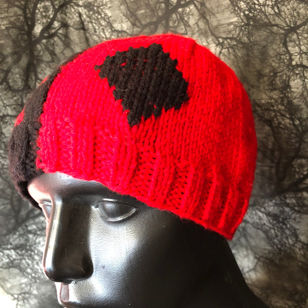 Side view of knit hat on a mannequin bust.This side is red with a black diamond on it.