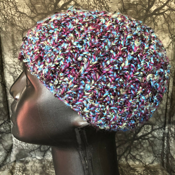 Side view of a multi-colored knit hat on a mannequin bust. The colors in the hat distributed all throughout instead of shifting colors that make stripes.